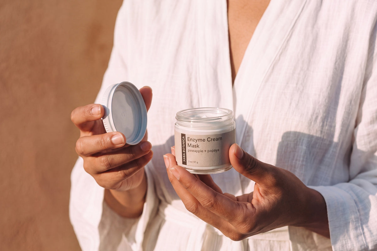 Woman in a white linen robe holding an open jar of Enzyme Cream Mask